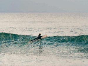 A person is seen paddling a surfboard on the waves in the ocean