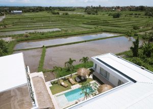 Aerial view of a surf camp at Kavo Maison with a swimming pool and vast green rice fields surrounding it