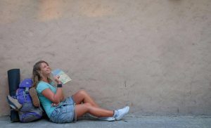 A female tourist is seen sitting with her back against an outdoor wall, taking a break