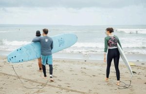 Three people on the beach getting ready to surf