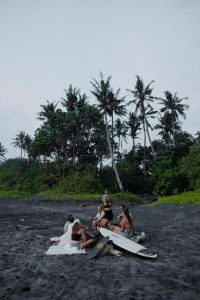 A group of people is gathered on the black-sand beach