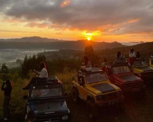 A group of tourists is enjoying the sunrise at Mount Batur from a jeep