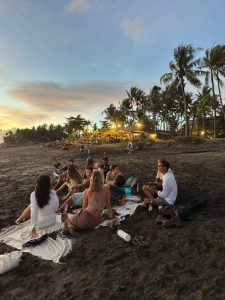 A group of people enjoying a leisurely picnic on the black-sand beach at sunset