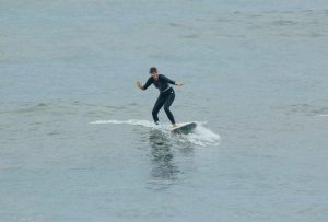 A person skillfully riding a wave on a longboard, wearing a full black wetsuit for warmth