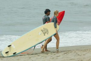 People walking on a beach while carrying Toras surfboards
