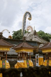 The atmosphere of a religious ceremony at a temple in Bali, decorated with yellow-and-white cloth and tall, curved bamboo penjor poles