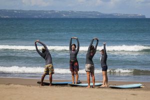 a group of people doing warm-up stretches on a sandy beach next to their surfboards before heading into the ocean