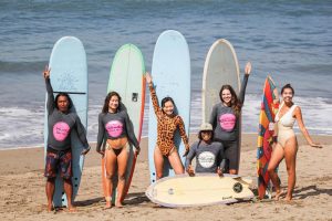 a group of people smiling and posing on a sunny beach with several longboards