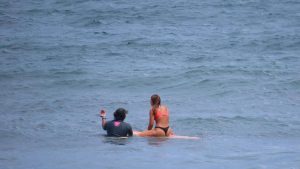 a person receiving instructions from a surf teacher while sitting on a longboard in the ocean