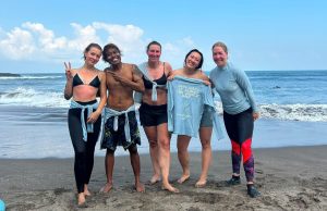 a group of people posing on a dark sand beach with the ocean in the background