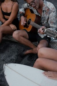 a man playing an acoustic guitar on a black-sand beach with his friends