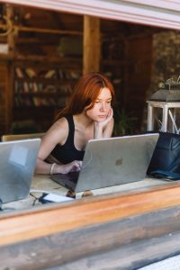 A woman with reddish-brown hair working on a silver Apple MacBook in a cozy