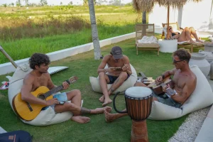 Guests playing guitars beside rice fields at Kavo Maison surf camp in Bali.