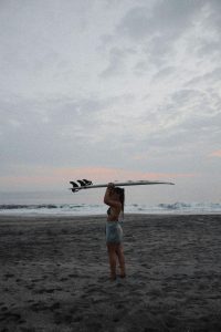 Surfer holding a surfboard overhead on a black sand beach in Bali at dusk