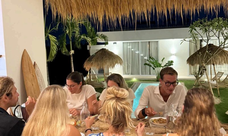 A group of people are enjoying dinner together in the dining area at Balisurfcamp Kavomaison.
