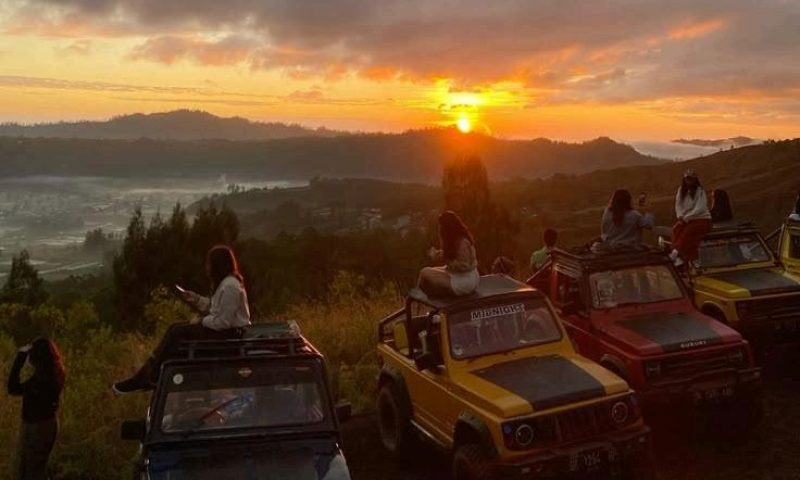 A group of tourists is enjoying the sunrise at Mount Batur from a jeep