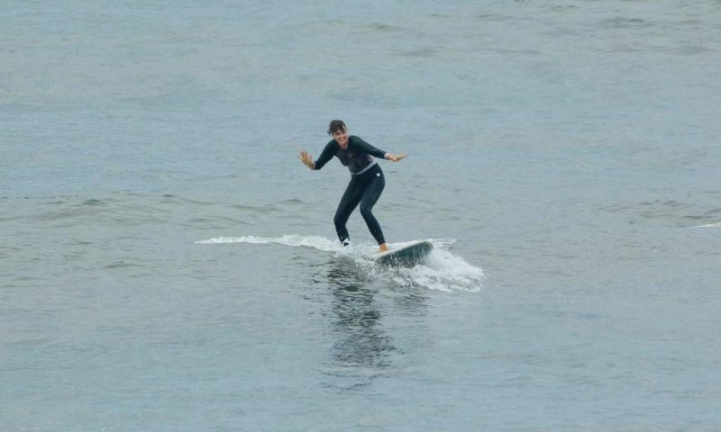 A person skillfully riding a wave on a longboard, wearing a full black wetsuit for warmth