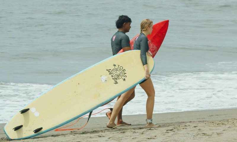 People walking on a beach while carrying Toras surfboards