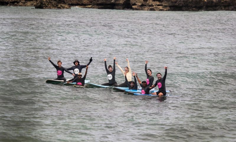 a group of people smiling and waving while floating on surfboards in the water